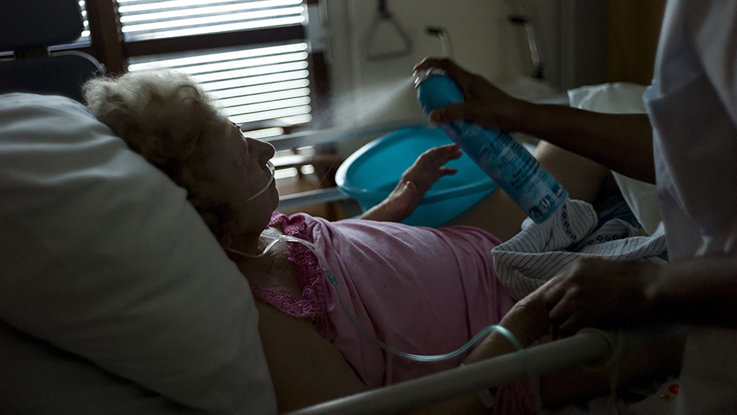 Foto einer alten Frau im Krankenhaus, die im Bett liegt und mit einem kühlenden Nebel bestäubt wird.